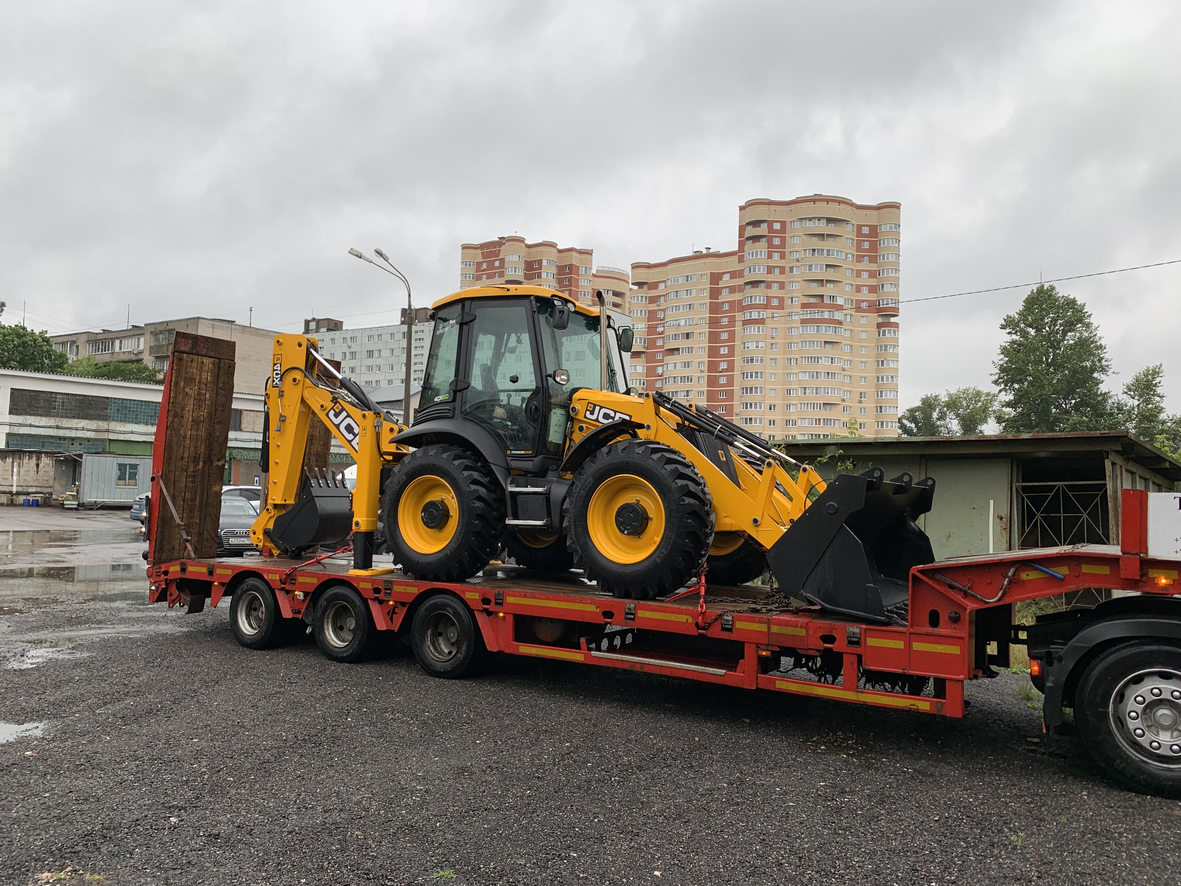 Sikker transport av gul gravemaskin lastet på rød maskintralle, som illustrerer optimal vektfordeling ved bruk av brønnhengere.